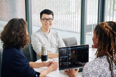 Asyalı genç adam, profesyonel borsa simsarlarıyla ofisinde görüşüyor ve tavsiye istiyor.