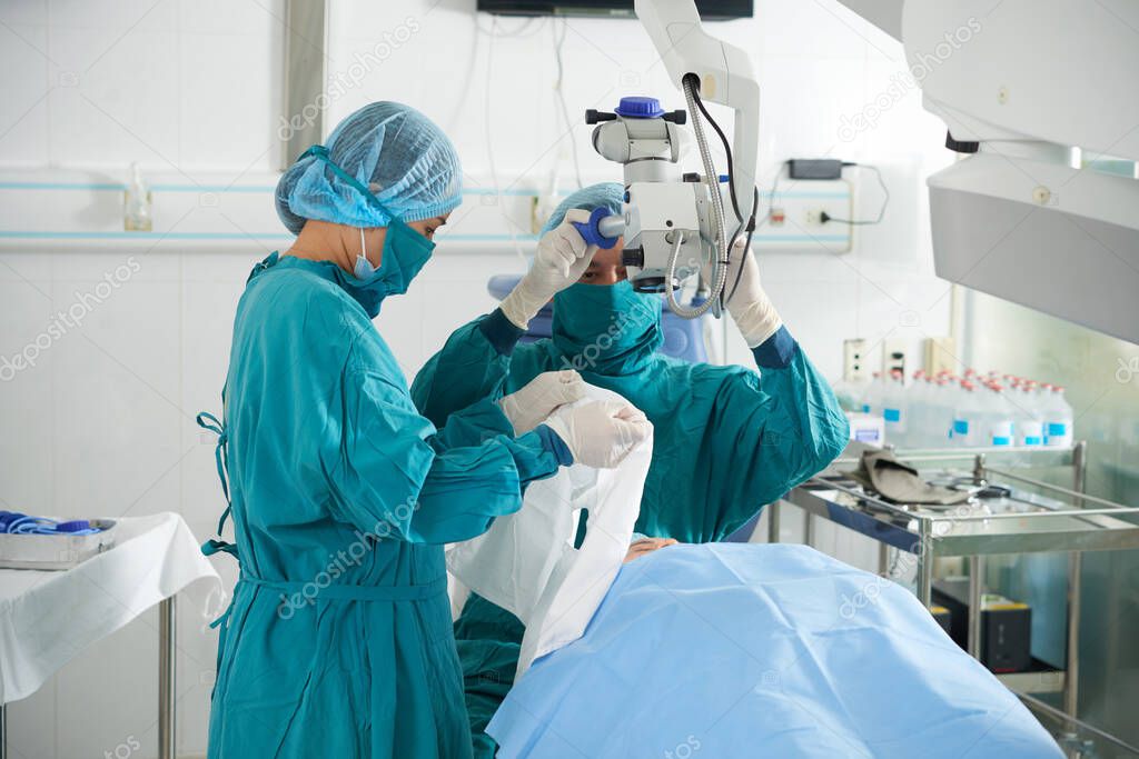 Surgeon and assistant preparing patient for vision restoration procedure