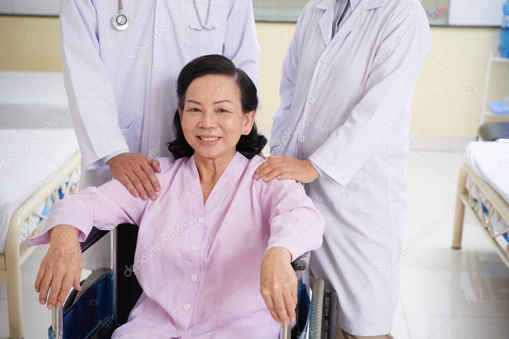 Happy Asian senior woman sitting in wheelchair after laser eye surgery with doctors standing near by