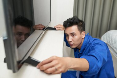 Ciddi bir servis çalışanı otel odasındaki konsola televizyon koyuyor.