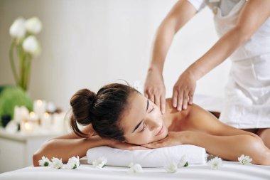 Güzel genç bir kadın spa salonunda yatakta dinleniyor ve sırt masajı yaptırıyor.