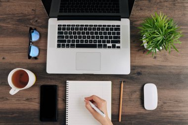 Dizüstü bilgisayarda webinar izleyen ve ders kitabında önemli detaylar yazan kadın