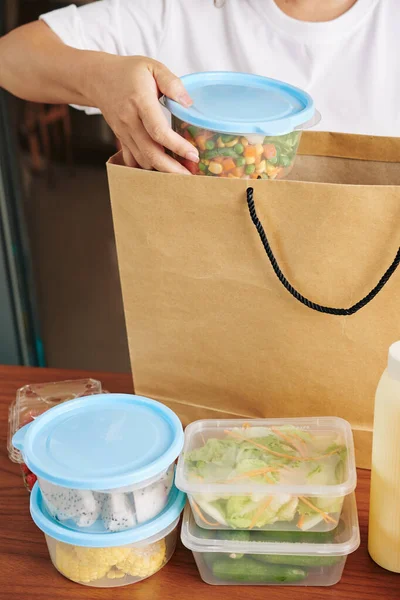 妇女从网上商店的大纸袋中取出装有新鲜沙拉的容器和切下水果的剪影 — 图库照片