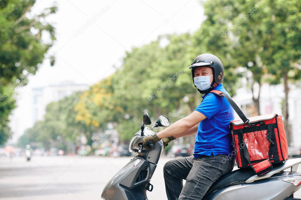 Cheerful courier riding on scooter when delivering food to customers during pandemic period