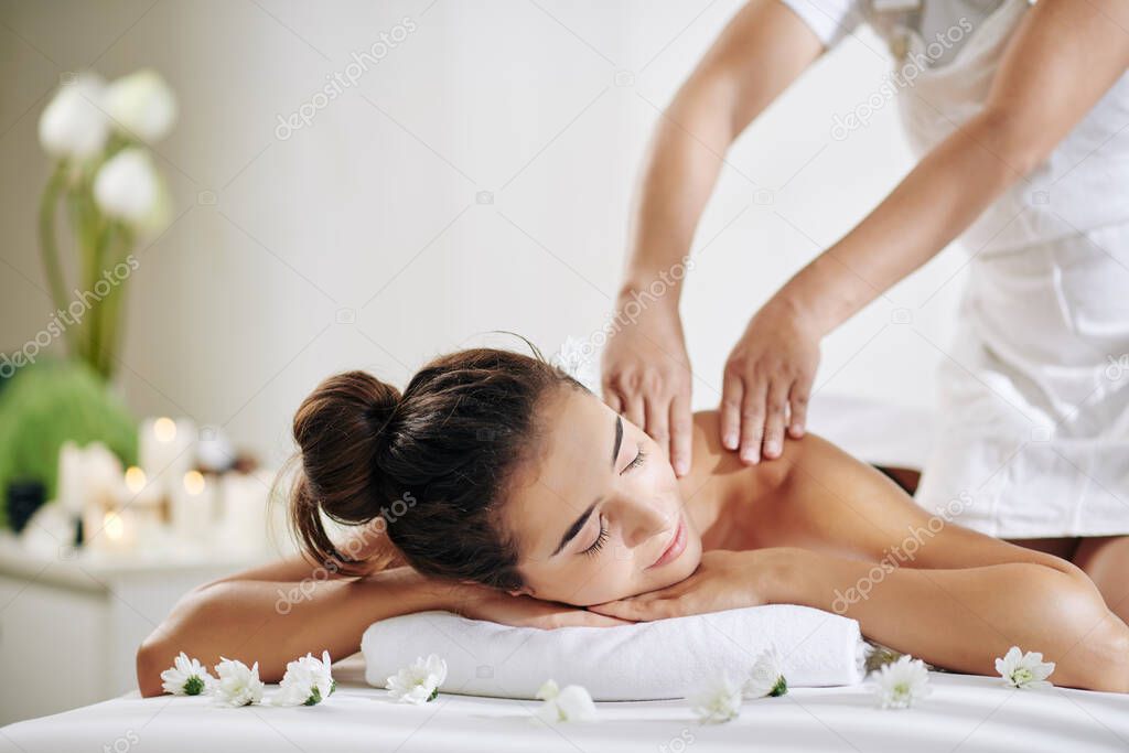 Pretty young woman relaxing on bed in spa salon and getting back massage