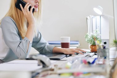 Bilgisayarda çalışan ve iş arkadaşı veya müşteriyle telefonda konuşan genç iş kadınının kırpılmış görüntüsü