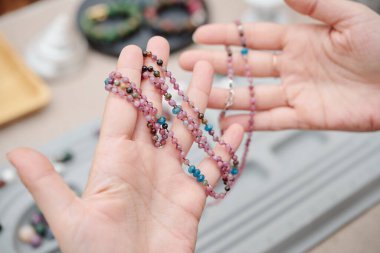 Onu yaratan kadının ellerinde küçük doğal taşlardan yapılmış güzel bir kolye.