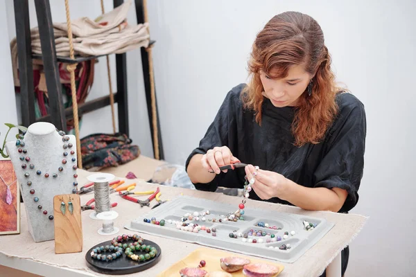 Young woman concentrated on making jewelry and using pliers to attach hook