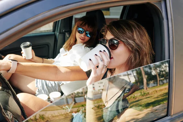 助手席で友人と車を運転するときにコーヒーを楽しむ正の若い女性 — ストック写真