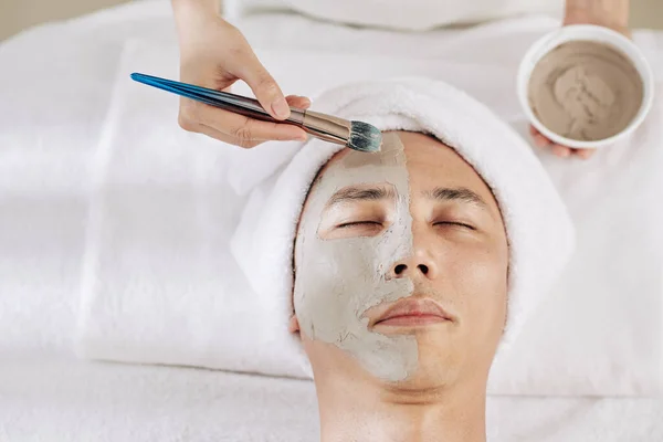 Kosmetolog Nakładający Glinianą Maskę Połowę Twarzy Męskiego Klienta — Zdjęcie stockowe