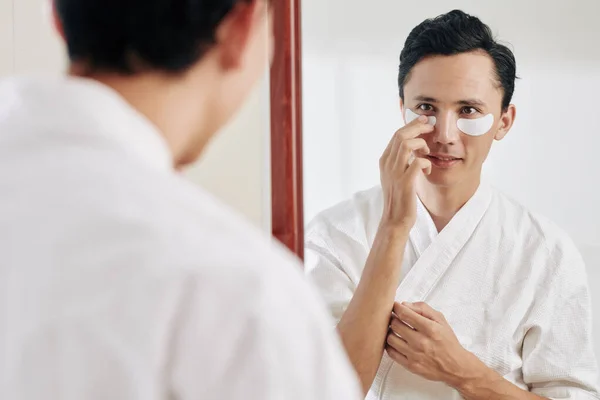 Smiling Man Waffle Bath Robe Looking Mirror Applying Eye Patches — Stock Photo, Image