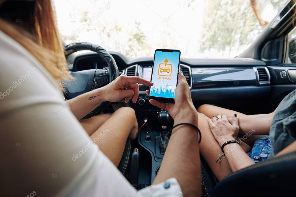 Female driver and passenger checking car sharing application on her smartphone