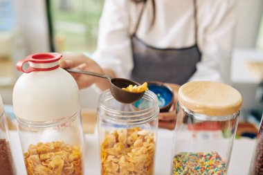 Garson kaseyi organik mısır gevreği ile doldururken plastik kaşık kullanıyor.
