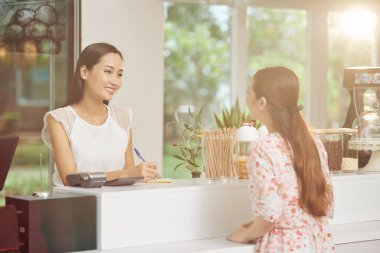 Gülümseyen güzel bayan barista tezgahta duruyor ve genç müşterilerin siparişlerini yazıyor.