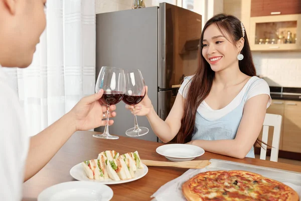 年轻的越南夫妇在家里与三明治和披萨共进晚餐时碰碰酒杯 — 图库照片