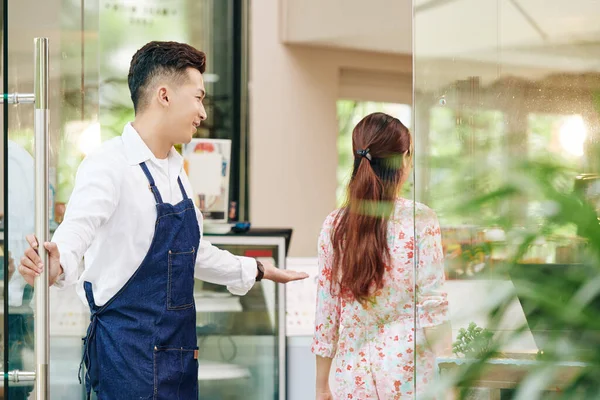 Kot Önlüklü Gülümseyen Garson Kadın Müşteriye Kafenin Kapısını Açıyor — Stok fotoğraf