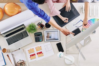 Bir grup iç mimar meslektaşlarının çalışmalarını eleştiriyor, bilgisayar ekranına işaret ediyor ve nasıl düzeltileceğine dair tavsiyelerde bulunuyor