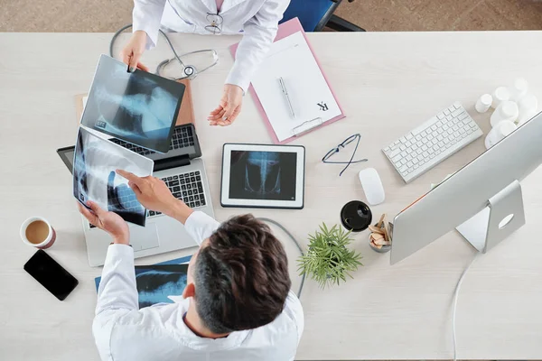 Doctors sitting at table and discussing chest x-rays of patients with pneumonia, view from above