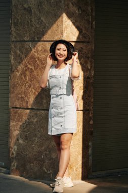 Küçük şapka ve kot elbiseyle poz veren sevimli Vietnamlı genç kadın.