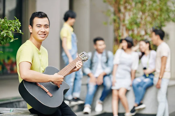 一个英俊的年轻亚洲学生在他大学的后院弹吉他 — 图库照片