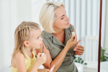 Anne aynanın önüne sıvı ruj sürüyor ve kızı ondan sonra tekrar ediyor.