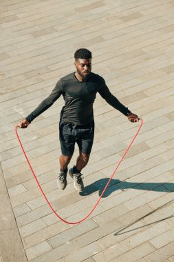 Konsantre olmuş zinde genç sporcu dışarıda antrenman yaparken ip atlıyor.