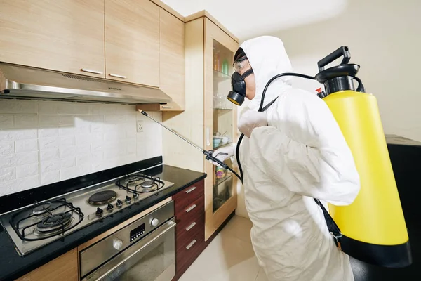 传染病的防治与流行观念的控制 穿着白色防护服在厨房橱柜上洒洗涤剂的工人 — 图库照片