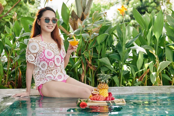 매력적 여성에게 오렌지 주스를 마시고 호텔에서 수영장에서 휴식을 과일을 — 스톡 사진