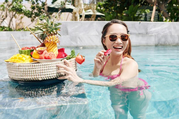 快乐漂亮的年轻女子站在游泳池里 享受着一片鲜红的激情水果 — 图库照片
