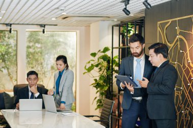 Ciddi genç sakallı iş adamı tablet bilgisayarında iş arkadaşına mali tabloyu gösteriyor.
