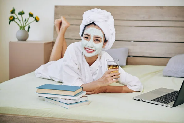 お茶を飲み 読書をし マスクで宿題をするバスローブの若いアジア人女性の肖像画 — ストック写真