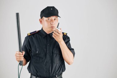 Studio photo of serious police officer raising hand with truncheon and talking to chief of police via walkie-talkie clipart