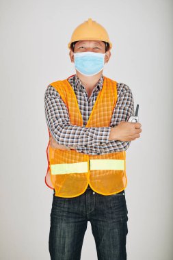 Güvenlik yeleği ve sağlık maskesi takmış, elinde telsizle kameraya bakan pozitif müteahhitlerin portresi.