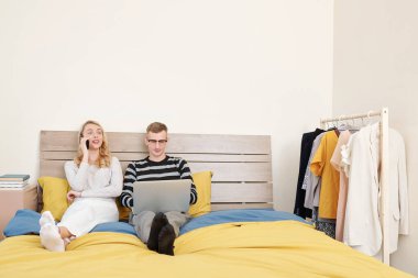 Çift bütün gün yatakta kalıyor, adam dizüstü bilgisayarla çalışıyor ve kadın müşterilerle telefon görüşmesi yapıyor.