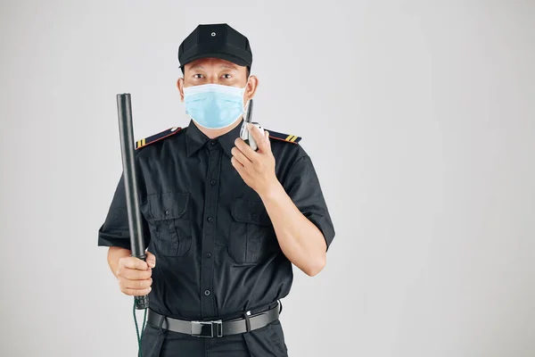 戴医疗面罩的保安人员手持警棍和对讲机交谈的肖像 — 图库照片