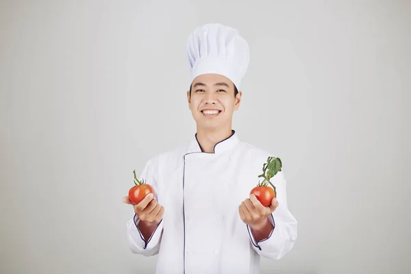 穿着制服拿着新鲜成熟西红柿的快乐英俊年轻厨师的画像 — 图库照片