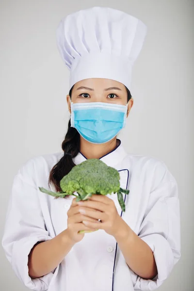 Jovem Chef Café Feminino Máscara Médica Segurando Brócolis Frescos — Fotografia de Stock