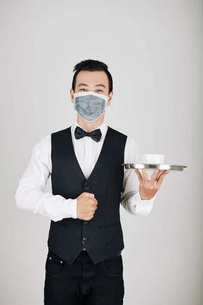 戴着医疗面罩的英俊快乐的年轻侍者 带着金属盘子里的咖啡 — 图库照片