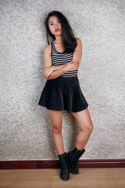 Dikey vücut stüdyosu modern Asya modelinin portresi şık mini etek, çizgili üst ve botlar giyerek gri duvar arkasında kameraya poz veriyor.