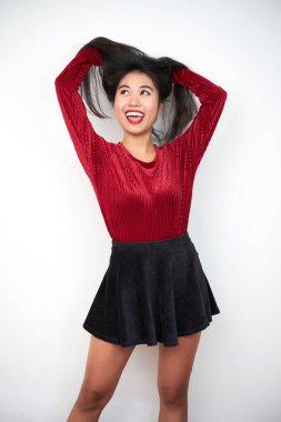 Koyu kırmızı bluz ve siyah mini etek giyen çekici Asyalı kadının dikey orta boy portresi beyaz arka planda kamerada poz verirken eğleniyor.