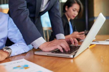 Tanımlanamayan bir adam masada dizüstü bilgisayarında bir şey yazıyor, iş arkadaşları yanında çalışıyor.