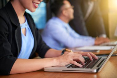 Ofiste iş arkadaşlarıyla oturmuş laptopuna bir şeyler yazan tanınmayan bir kadın.