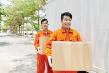 Turuncu üniformalı ve beyaz eldivenli neşeli servis elemanları müşteriye kutu taşıyorlar.