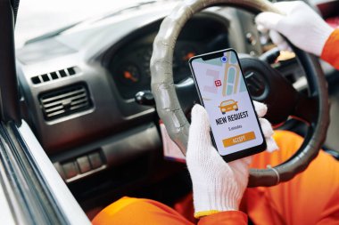 Teslimatçı arabada oturuyor. Akıllı telefonundan yeni iş isteği alıyor. Yatay yakın çekim.