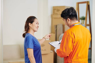 Yetişkin bir Asyalı kadının, teslimat görevlisine notlar alırken sorular sorduğu yatay bir fotoğraf.