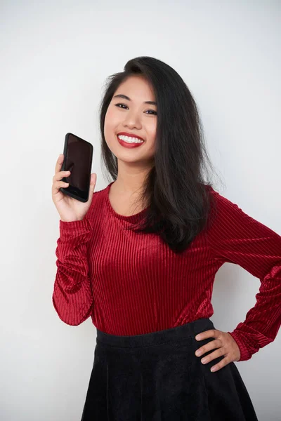 現代的なスマートフォンを持っている魅力的な若いアジアの女性の垂直スタジオの肖像画カメラの笑顔 白い背景を見て — ストック写真