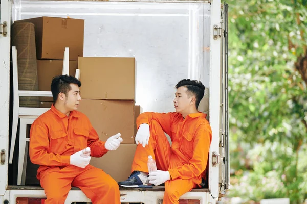 Two men working together in house moving service sitting together drinking water and talking while having break