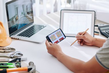 İç mimar ofis masasında oturuyor ve tadilat projesinde çalışırken evin resimlerini ve fotoğraflarını kontrol ediyor.