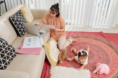 Küçük bir kızla evde kalırken, Asyalı genç bir iş kadını mali belgelerle çalışıyor.