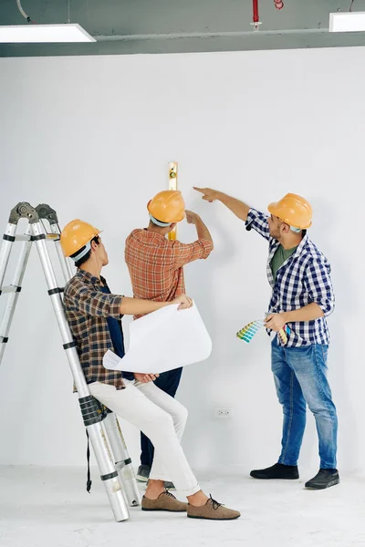 Trabalhadores Manuais Modernos Vestindo Chapéus Amarelos Verificando Nível Parede Sala — Fotografia de Stock